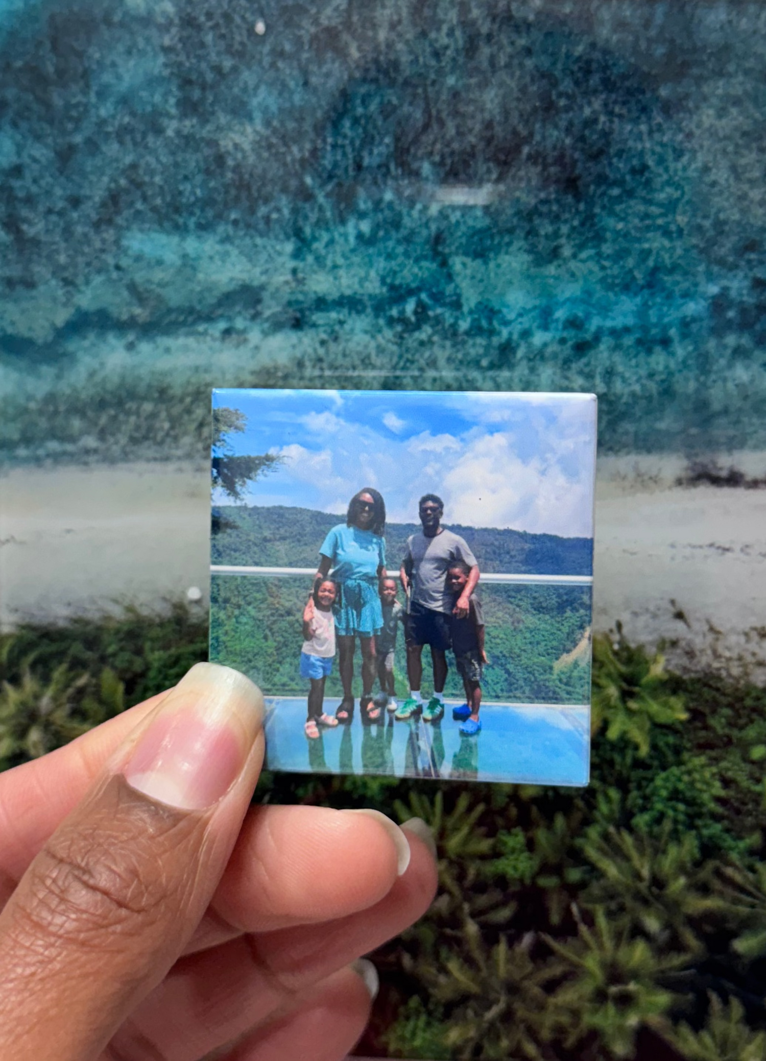 Hand holding a small photo of a family by a pool against a textured white wall.
